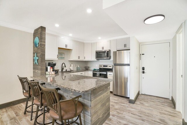 kitchen with kitchen peninsula, light stone countertops, stainless steel appliances, sink, and white cabinetry