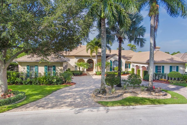 view of front of home with a tile roof, a front lawn, decorative driveway, and stucco siding