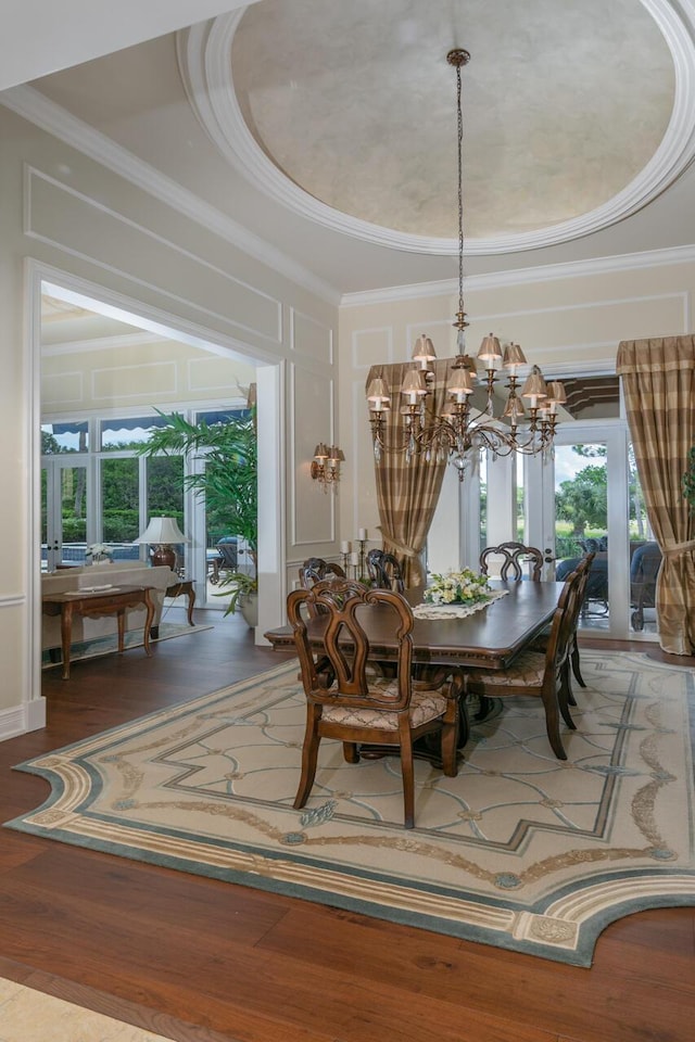 dining space featuring a raised ceiling, an inviting chandelier, wood finished floors, and crown molding