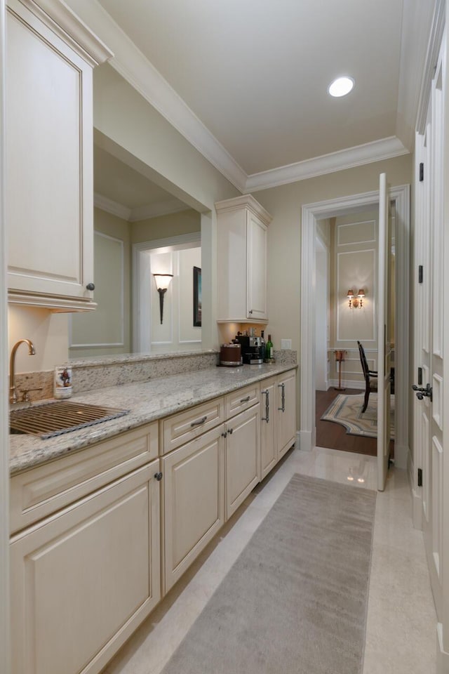 kitchen with light tile patterned floors, cream cabinets, a sink, light stone countertops, and crown molding