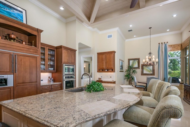 kitchen featuring pendant lighting, stainless steel appliances, brown cabinetry, light stone countertops, and a large island with sink