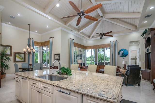 kitchen with light stone counters, a sink, open floor plan, an island with sink, and pendant lighting