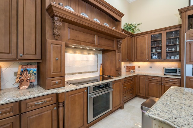 kitchen featuring black electric stovetop, oven, light stone countertops, open shelves, and glass insert cabinets