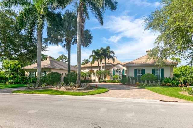 view of front facade with a front yard, decorative driveway, a chimney, and stucco siding