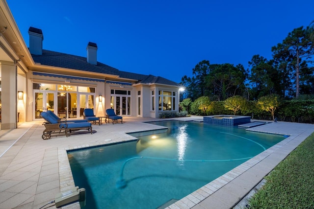 pool at twilight with a pool with connected hot tub, french doors, and a patio