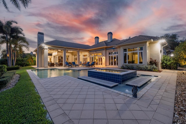 pool at dusk featuring ceiling fan, an in ground hot tub, french doors, an outdoor pool, and a patio area