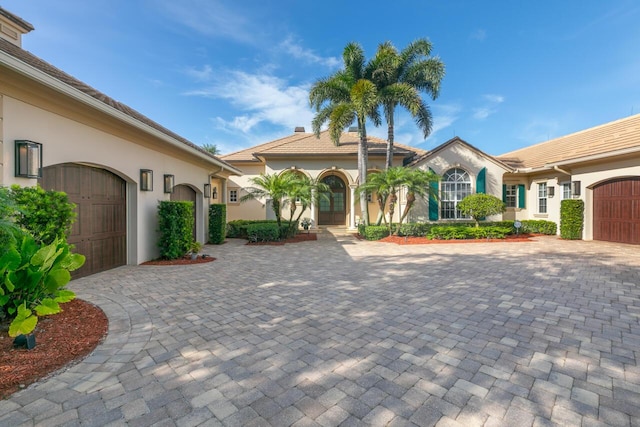 view of front of home with a garage, decorative driveway, a chimney, and stucco siding