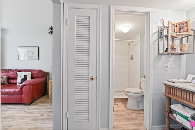 bathroom featuring a tile shower, wood-type flooring, and toilet