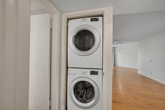 clothes washing area featuring a textured ceiling, stacked washing maching and dryer, and light hardwood / wood-style floors