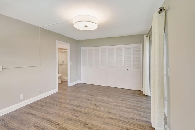 unfurnished bedroom with hardwood / wood-style floors, ensuite bathroom, and a closet