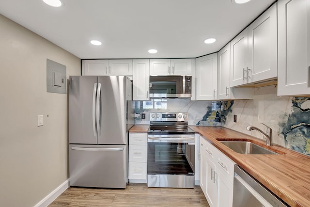 kitchen with wood counters, appliances with stainless steel finishes, sink, light hardwood / wood-style flooring, and white cabinetry