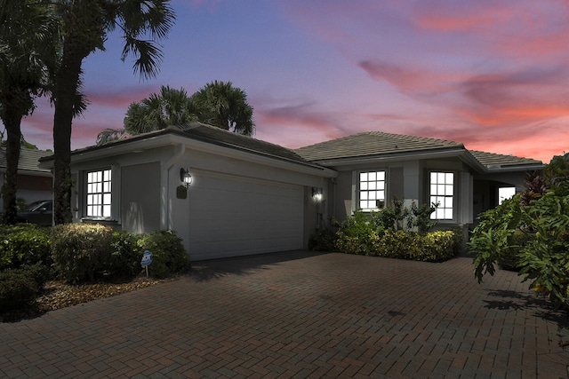 view of front of home featuring an attached garage, stucco siding, decorative driveway, and a tiled roof