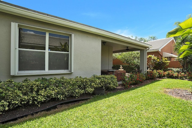 view of side of home with stucco siding, a lawn, and a ceiling fan