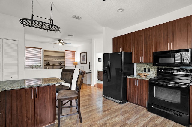 kitchen with black appliances, light wood-style flooring, a breakfast bar area, tasteful backsplash, and a textured ceiling