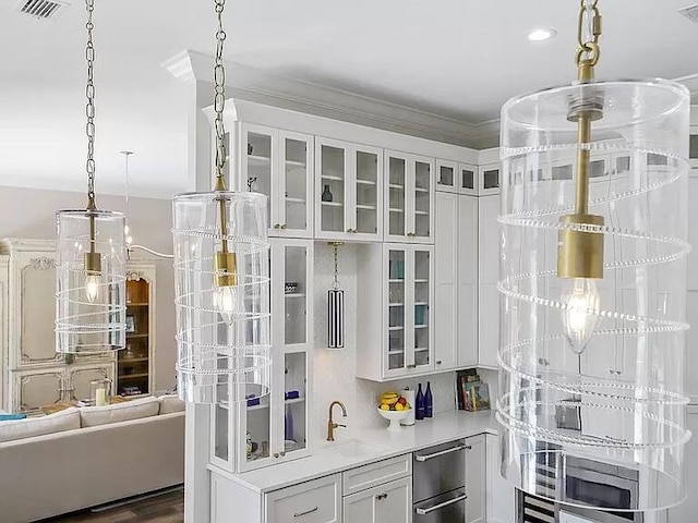 interior space with visible vents, ornamental molding, glass insert cabinets, white cabinets, and a sink