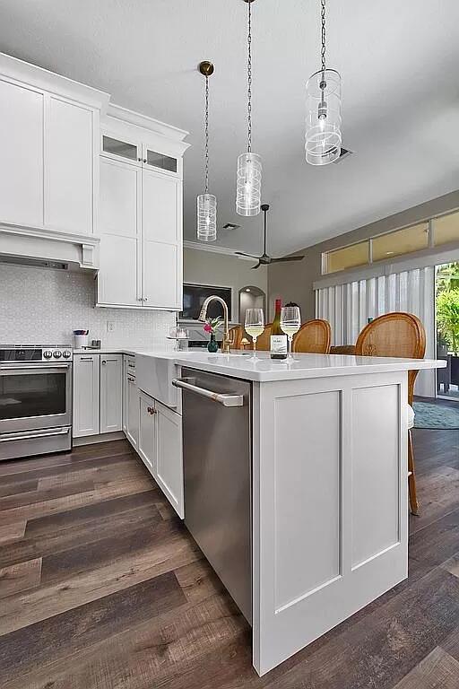 kitchen featuring dark wood finished floors, wall chimney exhaust hood, appliances with stainless steel finishes, a peninsula, and light countertops