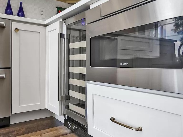 interior details featuring dark wood-type flooring, beverage cooler, white cabinetry, and oven