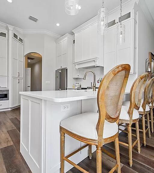 kitchen with arched walkways, dark wood finished floors, stainless steel appliances, light countertops, and a kitchen bar