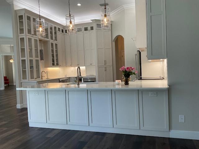 kitchen featuring arched walkways, a sink, light countertops, hanging light fixtures, and crown molding