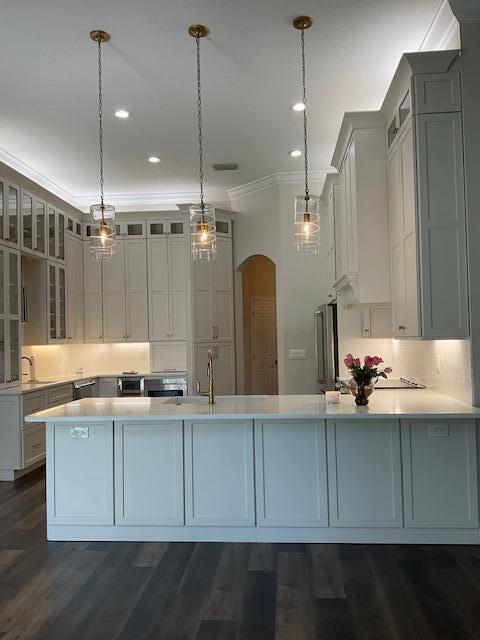 kitchen featuring arched walkways, light countertops, ornamental molding, glass insert cabinets, and a peninsula