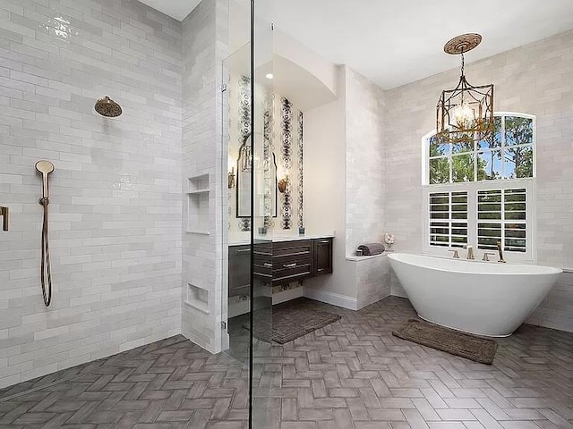 full bathroom with a notable chandelier, tile walls, a freestanding bath, vanity, and tiled shower