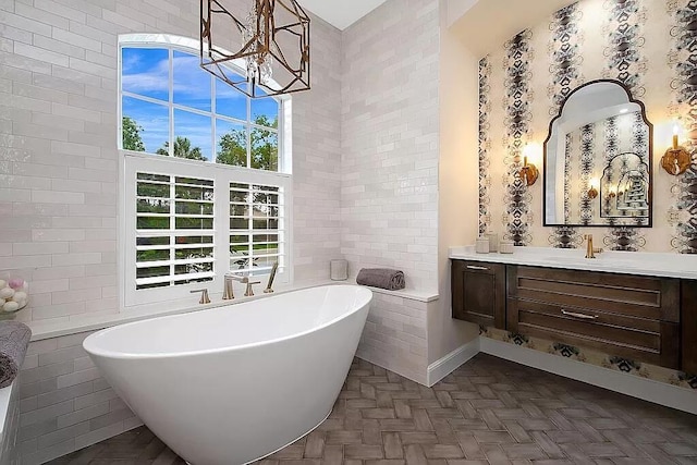 full bathroom featuring a notable chandelier, a soaking tub, vanity, and tile walls