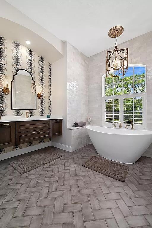 full bath with a notable chandelier, tile walls, a freestanding bath, and vanity