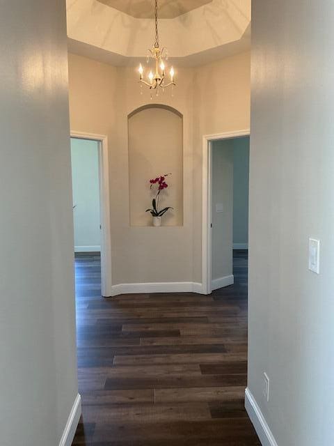 hallway with a chandelier, a high ceiling, baseboards, a tray ceiling, and dark wood finished floors