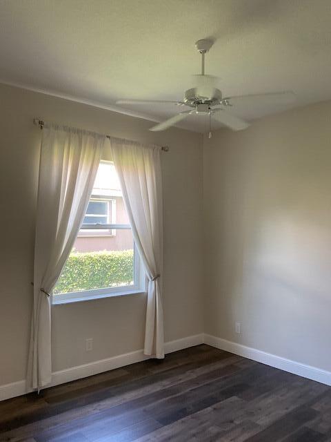 unfurnished room with dark wood-style floors, a ceiling fan, and baseboards