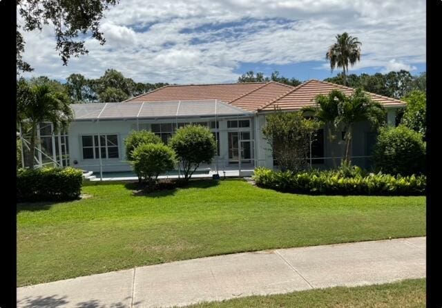 view of front facade featuring glass enclosure, a front yard, and a tile roof