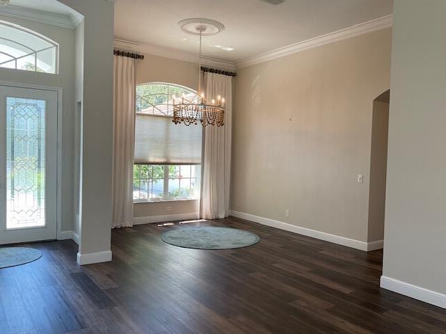 entrance foyer featuring ornamental molding, arched walkways, and dark wood-style flooring