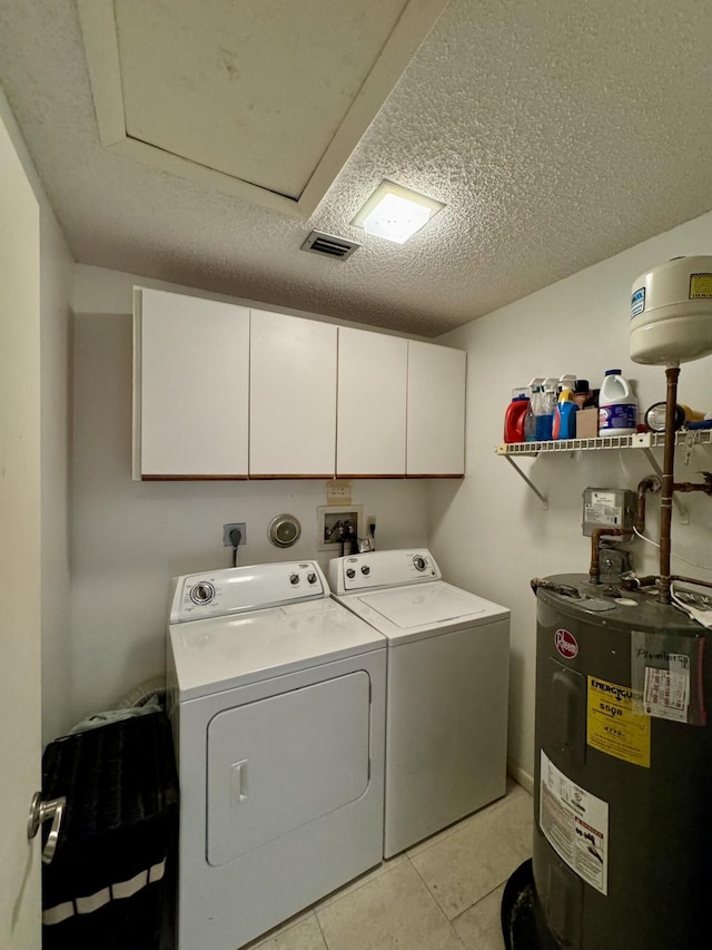 laundry room with washing machine and clothes dryer, cabinets, water heater, a textured ceiling, and light tile patterned flooring