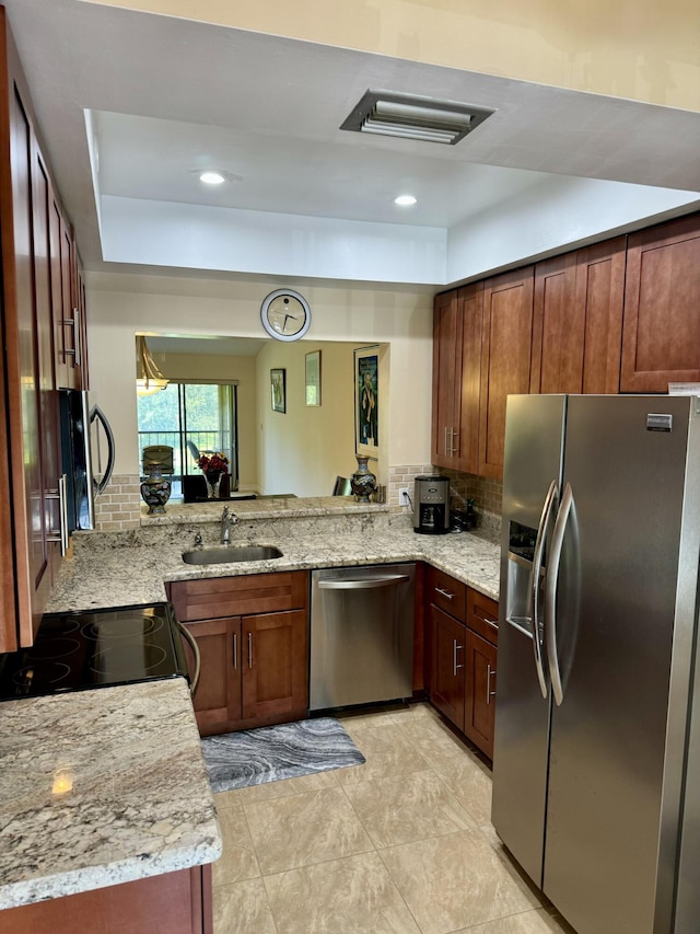 kitchen with kitchen peninsula, appliances with stainless steel finishes, light stone counters, and sink