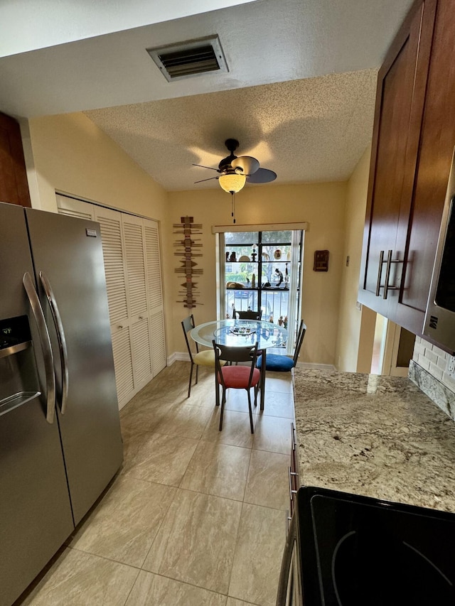 kitchen with a textured ceiling, ceiling fan, light stone counters, and stainless steel refrigerator with ice dispenser