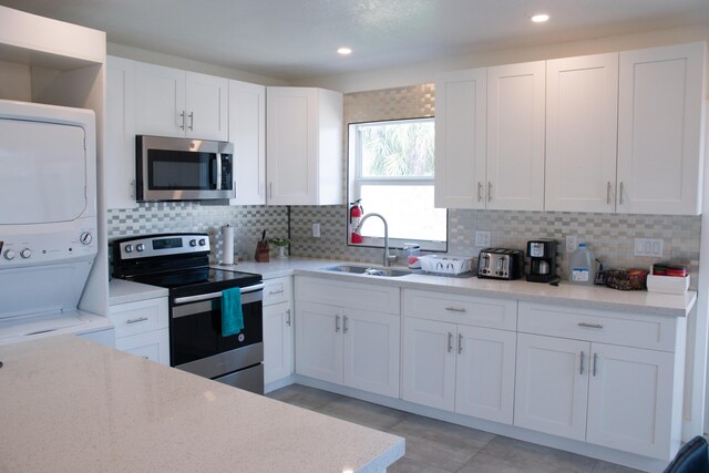 kitchen featuring white cabinetry, tasteful backsplash, stainless steel appliances, stacked washer and clothes dryer, and sink