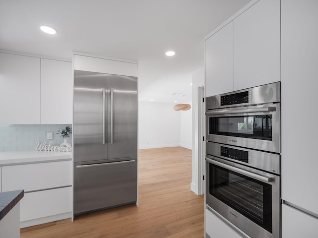 kitchen with appliances with stainless steel finishes, light hardwood / wood-style flooring, white cabinets, and tasteful backsplash