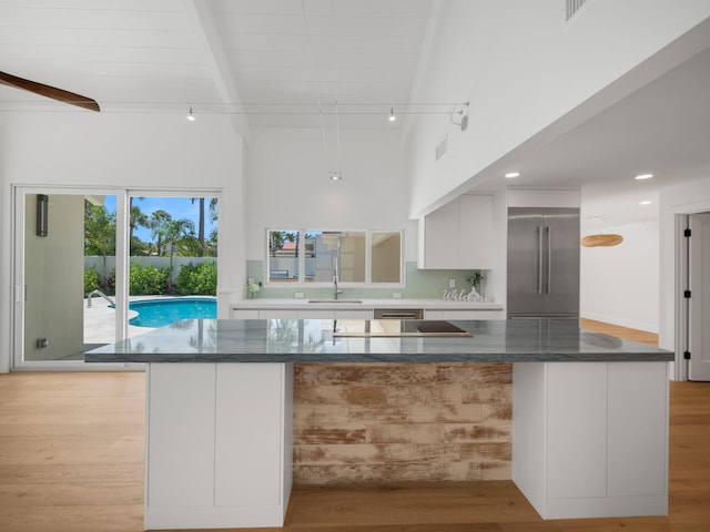 kitchen with dark stone countertops, beam ceiling, decorative backsplash, white cabinetry, and stainless steel built in refrigerator