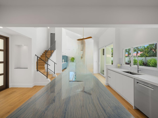 kitchen with stainless steel dishwasher, white cabinets, sink, and light hardwood / wood-style floors