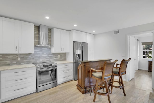 kitchen with tasteful backsplash, white cabinetry, wall chimney range hood, and appliances with stainless steel finishes