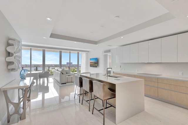 kitchen with a raised ceiling, sink, white cabinetry, a kitchen bar, and an island with sink