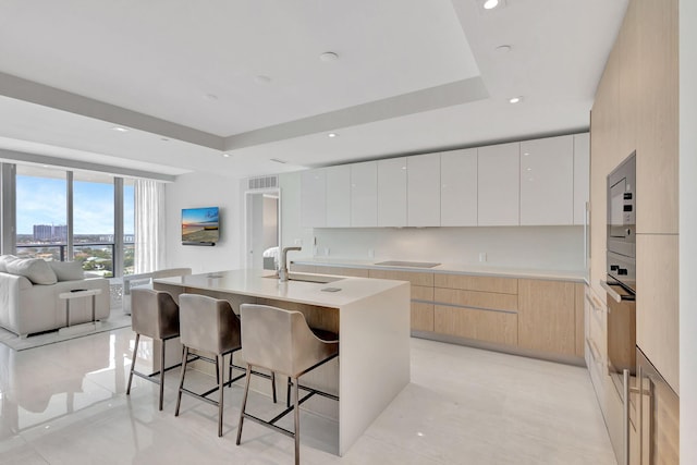 kitchen featuring white cabinets, sink, a kitchen island with sink, a tray ceiling, and a breakfast bar area