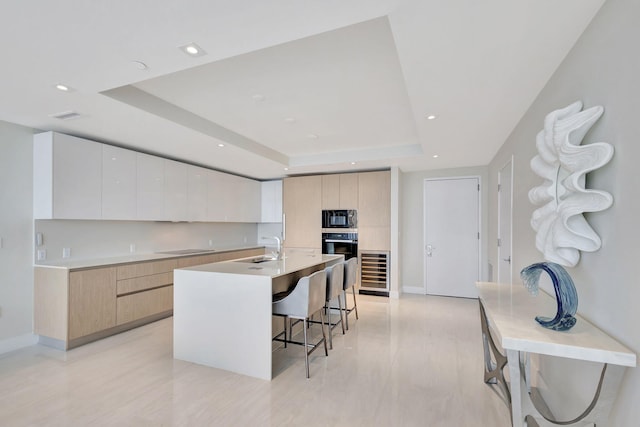 kitchen featuring black appliances, a raised ceiling, wine cooler, and an island with sink