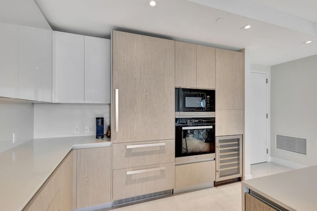 kitchen featuring light brown cabinetry, wall oven, built in microwave, and wine cooler