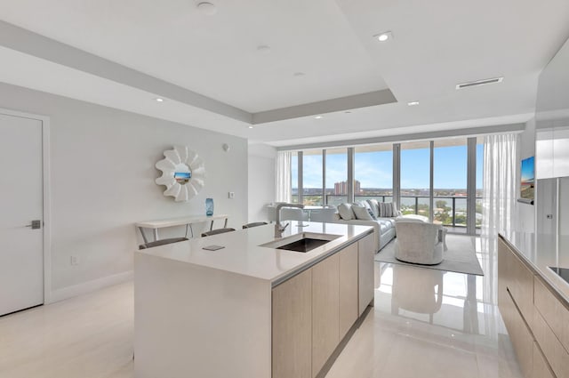 kitchen featuring light tile patterned floors, sink, a raised ceiling, floor to ceiling windows, and an island with sink