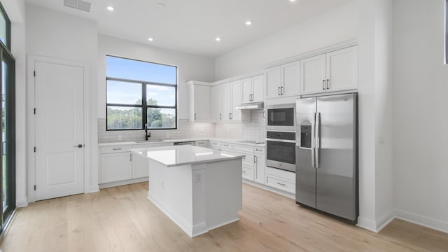 kitchen with white cabinetry, a center island, decorative backsplash, appliances with stainless steel finishes, and light wood-type flooring