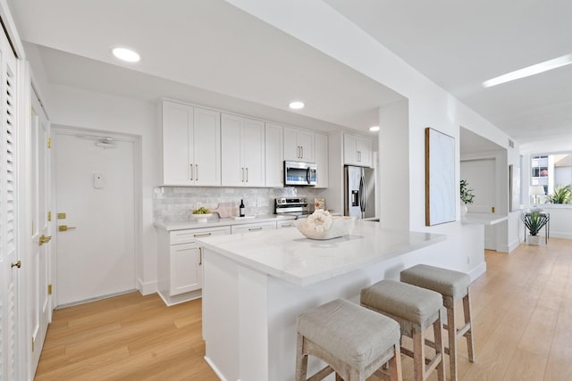 kitchen featuring white cabinetry, light hardwood / wood-style flooring, backsplash, stainless steel appliances, and a kitchen breakfast bar