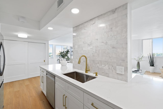 kitchen featuring white cabinetry, light wood-type flooring, light stone counters, stainless steel dishwasher, and sink