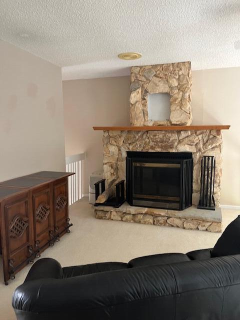 living room with a stone fireplace, carpet flooring, and a textured ceiling