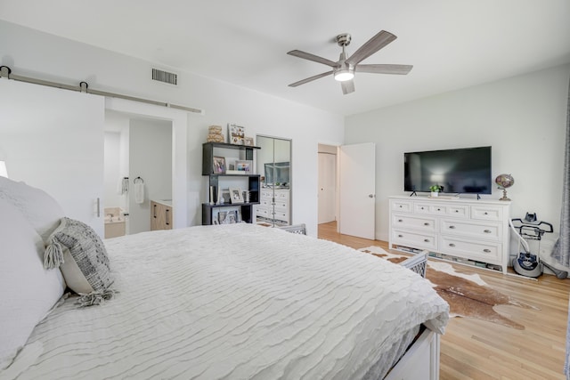 bedroom with a barn door, light hardwood / wood-style floors, and ceiling fan