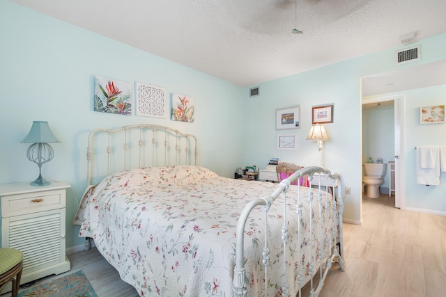 bedroom featuring ceiling fan, light hardwood / wood-style flooring, ensuite bath, and a textured ceiling